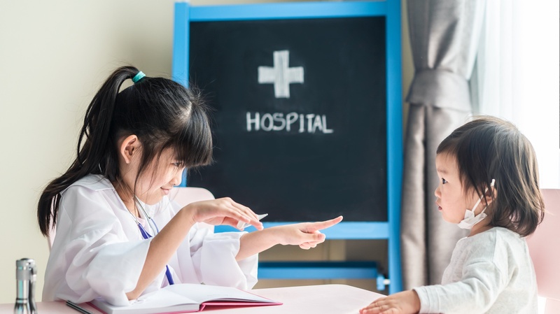 Zwei asiatisch gelesene Mädchen spielen in der Spitalschule Patientin und Ärztin