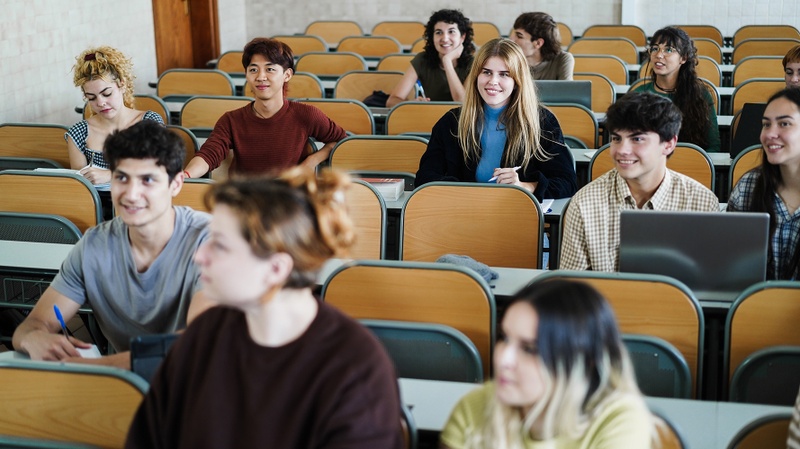 Studierende in einem Hörsaal hören lächelnd zu