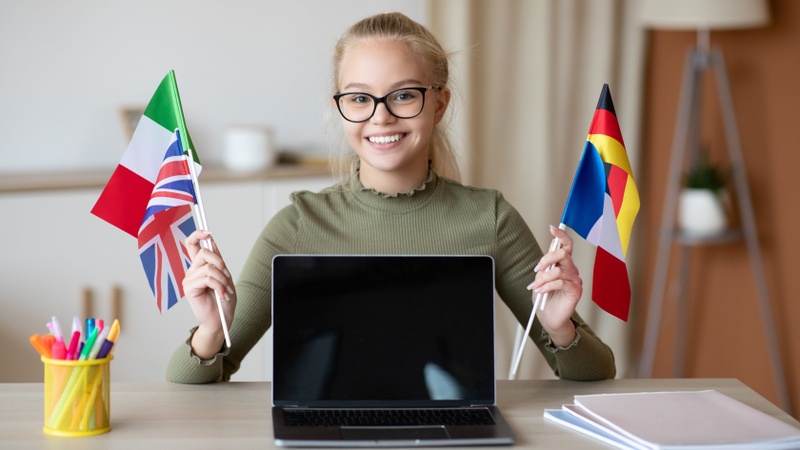 Fröhliches Schulmädchen mit Flaggenbündel zeigt Laptop