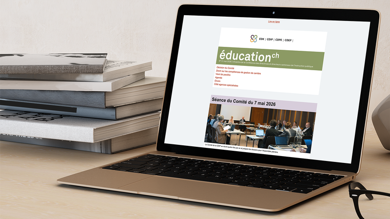 Laptop ouvert, montrant l’infolettre de la CDIP sur son écran; pile de livres posée à gauche du laptop