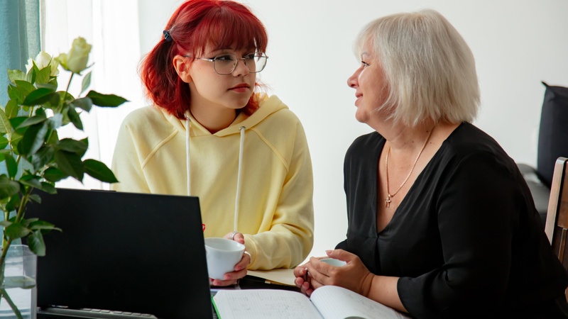 Une femme et une jeune femme discutent ensemble devant un bureau équipé d'un ordinateur et de notes