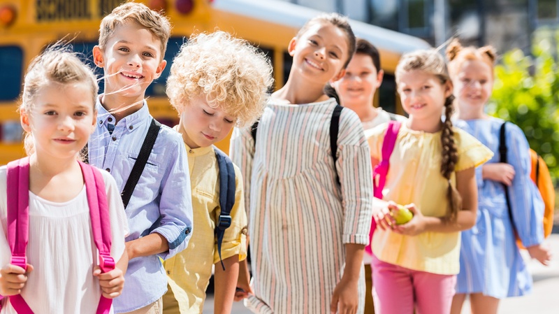 Des écoliers sont alignés les uns derrière les autres devant un bus scolaire jaune