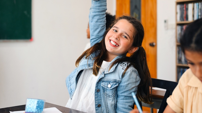 Une jeune élève lève la main et sourit avec enthousiasme